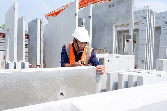 An industrial engineer uses a tape measure to measure a precast concrete wall.