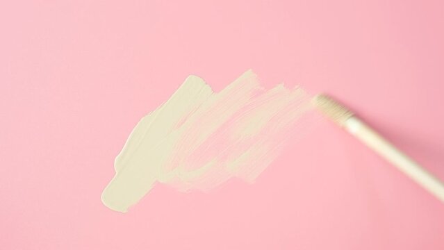 Smear with a brush of beige foundation or concealer on a pink background close-up.