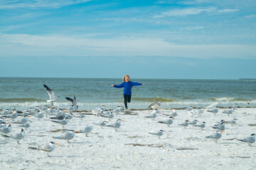 Happy childhood. Child and seagull on the beach. Amazed boy running on the beach with his hands raised up with flying seagulls birds.