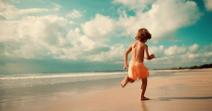 Boy playfully runs along the beach and looks back. Concept of kid have fun