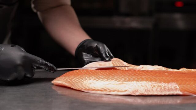 Salmon is in the hands of Japanese chef. He is using a knife to slice salmon fillet for sashimi and sushi. Ingredient for seafood dish.