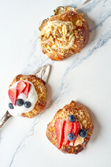 Three delicious buns with white sweet cream, nuts and berries. Sweet French pastries on a marble background