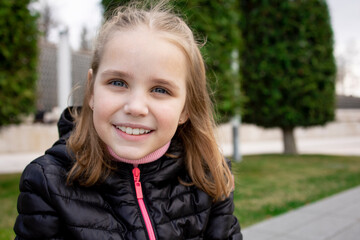 Portrait of a cute little girl with blonde hair and blue eyes walking in the park. Close-up. Place for text