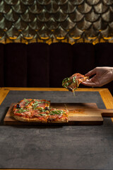 Hand taking pice of arugula prosciutto pizza served on a wooden board