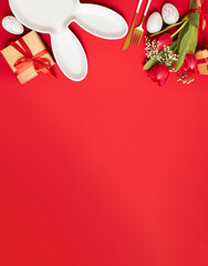 easter eggs, flowers, gifts and bunny plate with cutlery on a red bright background. easter frame layout. place for text. woopy space. flat lay. top view.