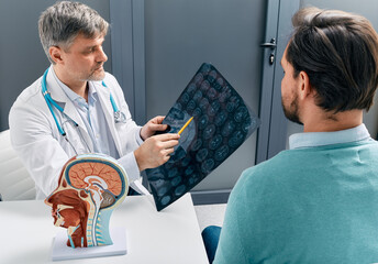 Doctor explaining to male patient results of MRI scan of his brain. Diagnosis of diseases and head...