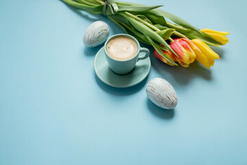 bouquet of yellow tulips, coffee in a blue cup, easter eggs  on a pastel blue background. copy...