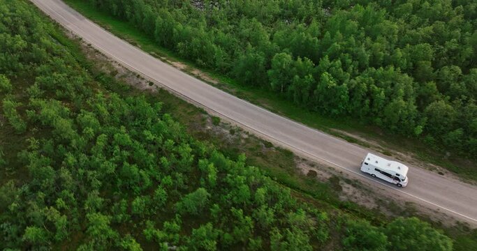 Aerial view tracking a RV driving in boreal forest on a summer day in Scandinavia