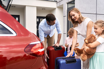 Caucasian family packing luggage into car trunk for holiday