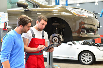 after-sales service in the car repair shop - mechanic and man talk about repairing a vehicle