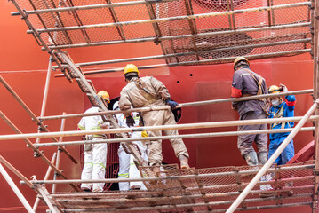 Dock yard, shipyard employees are working near the big container vessel hull. She is inside drydock for scheduled repairs and painting. 