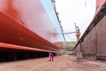 Inside dry dock, view on the bottom part of the big container ship newly painted to red colour. 
