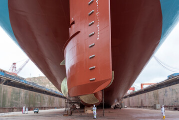 Aft view on the container ship inside dry dock, propeller on the first plan. Ship is inside a dry dock for routine maintenance and painting. - obrazy, fototapety, plakaty