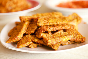Tempe goreng or fried tempeh is served on a plate along with sambal