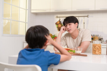 Obraz na płótnie Canvas Young Asian father angry his son about eat vegetables in kitchen at home