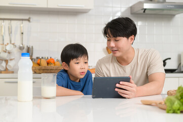 Young Asian father and his son using digital tablet enjoying together in kitchen at home