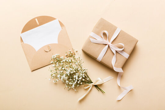 Wedding Mockup With White Paper List And Flowers Gypsophila On Colored Table Top View Flat Lay. Blank Greeting Cards And Envelopes. Beautiful Floral Pattern. Flat Lay Style