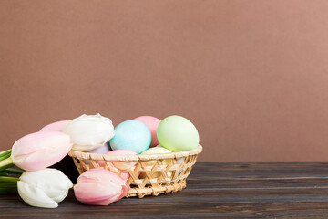 Happy Easter composition. Easter eggs in basket on colored table with yellow Tulips. Natural dyed colorful eggs background with copy space