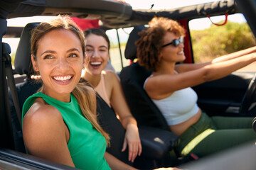 Group Of Laughing Female Friends Having Fun In Open Top Car On Road Trip