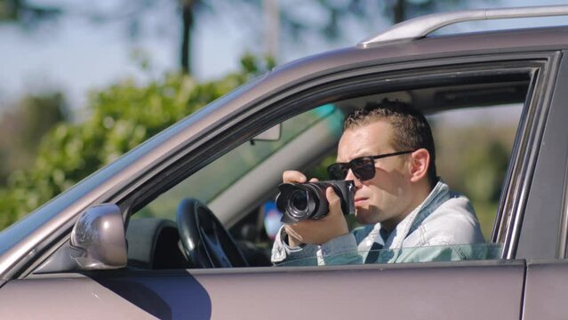 Man with camera sits inside car and takes pictures with professional camera, private detective or paparazzi spy. Journalist seeks synsation and follows celebrities.