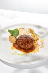 Beef cutlet with grilled cauliflower with gravy and cheese sauce on white plate. Elegant beefsteak on light background with shadows of sunlight. Summer menu with hard shadows Meat ball of minced meat