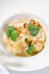 Seafood risotto with scallops and cauliflowers on white plate. Creamy risotto with sea scallops and cauliflowers. Italian risotto with sea scallops on light background with shadows of leaves