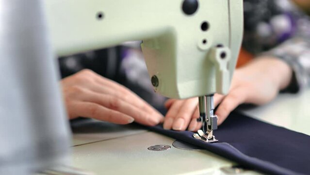 Female seamstress hands sews textile clothes use electric sewing machine tailoring atelier closeup