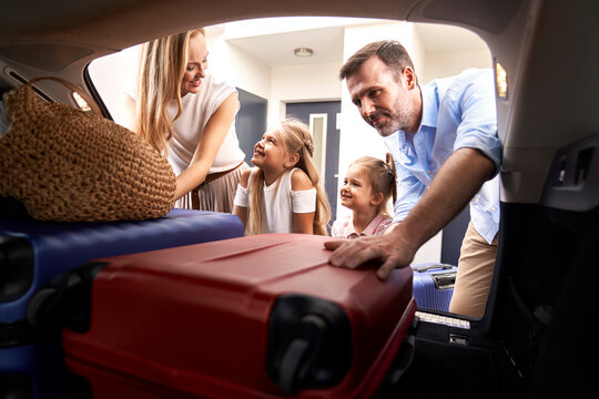 Caucasian family of four packing luggage into car trunk for holiday