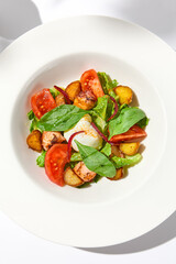 Salad with octopus, baked potatoes and poached egg on white table with hard shadows. Seafood salad with vegetables and potatoes in summer menu restaurant. Octopus and eggs salad in modern style.