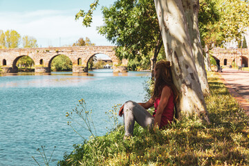 Woman tourist sitting and looking at ancient roman bridge in Merida city landscape- Estramadura