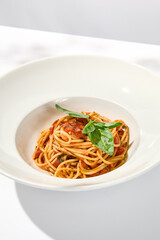 Vegetarian pasta with basil and tomatoes on white plate. Tomato pasta in summer menu with hard shadows Spaghetti with tomatoes on light background. Vegan food - spaghetti marinara