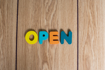 Top view of "OPEN" on colorful wooden blocks or cubes with wooden background. 
