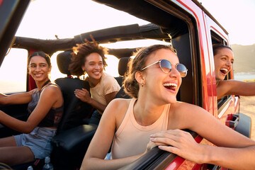 Group Of Laughing Female Friends Having Fun In Open Top Car On Road Trip