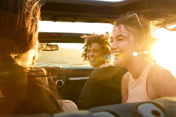 Group Of Laughing Female Friends Having Fun In Open Top Car On Road Trip