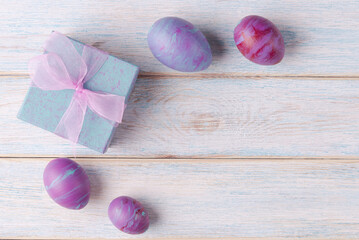 Painted Easter eggs and gift box on wooden background with copy space. Trendy fluid art decoration. Easter holiday concept