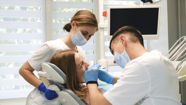 A dentist and an assistant examine the teeth of a female patient. Dental treatment in a modern clinic