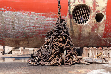 Anchor chain collected near ships hull. Ship is in a dry dock for scheduled repairs and painting. 