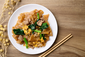 Thai food (Pad See Ew), Stir fried rice noodles soy sauce with pork, egg and kale on wooden background, Table top view