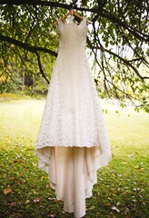 Vertical shot of a white wedding dress hanging from a branch of a tree