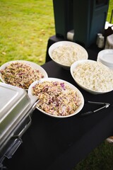 Vertical shot of food in white bowls on a black table in the middle of a green field