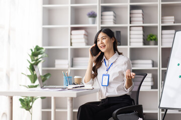 Cheerful business Asian woman freelancer making telephone call share good news about project working in office workplace, employee business finance concept.