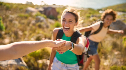 Fototapeta premium Group Of Female Friends With Backpacks Helping Each Other On Hike In Countryside On Coastal Path