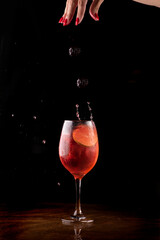 sexy female hand pouring red fruits into refreshing spritz cocktail with orange on dark background...