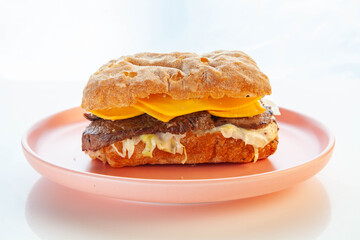 Philly cheese steak ciabatta sandwich served on a pink plate.