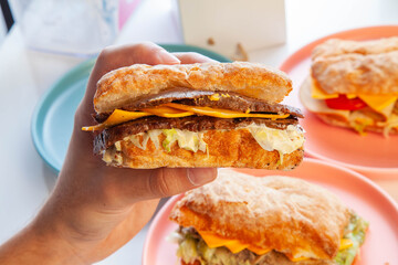 Philly cheese steak sandwich holding in hand with other sandwiches in background.