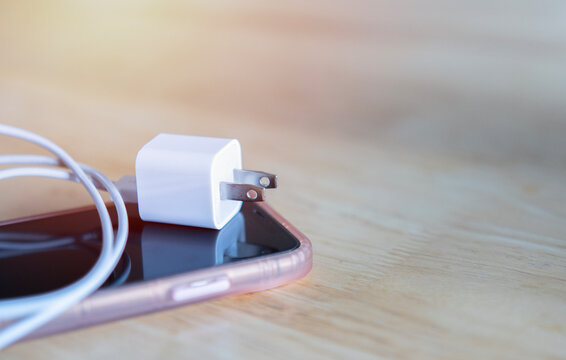 On a wooden table there is a cell phone and a charger with its USB cable.