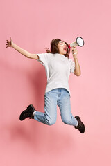 Full-length portrait of young girl in casual clothes emotionally shouting in megaphone in jump...