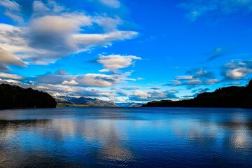 Scenic view of the sea before mountain slopes under a blue sky with clouds