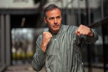 A middle-aged man is working out outdoors in the city, he is doing cardio exercises and boxing...