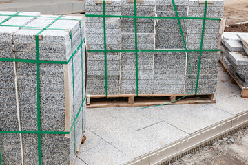 Packs of new paving granite tiles stacked on pallets for laying on the road.